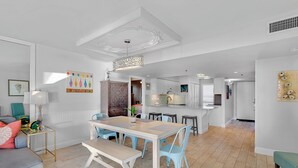 Una cocina moderna con armarios blancos, una isla central y una zona de comedor con mesa y sillas.