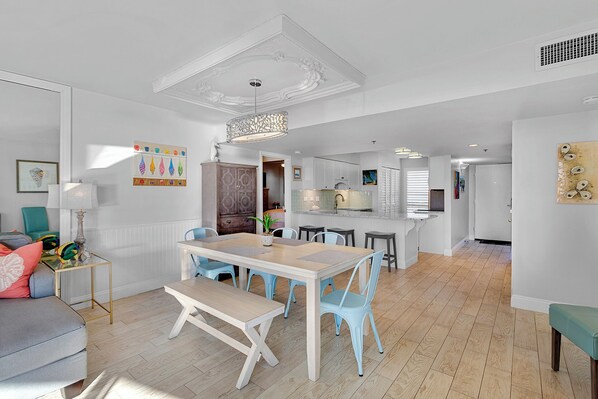 A modern kitchen with white cabinets, a central island, and a dining area with a table and chairs. - Mainsail 472 - Gulf Front Condo, Community Pool, Hot Tub, Free Beach Service! (Miramar Beach)