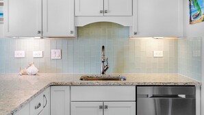Una cocina con armarios blancos, encimera de granito, pileta de acero inoxidable y lavavajillas.