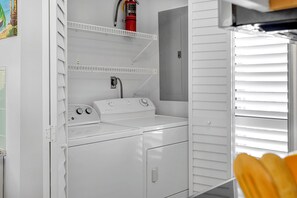 A laundry room with a front-loading washer and dryer, a fire extinguisher on the wall, and a door with a handle. - Mainsail 472 - Gulf Front Condo, Community Pool, Hot Tub, Free Beach Service! (Miramar Beach)