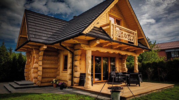 A log cabin with a balcony, a covered porch, and a patio area with outdoor furniture.