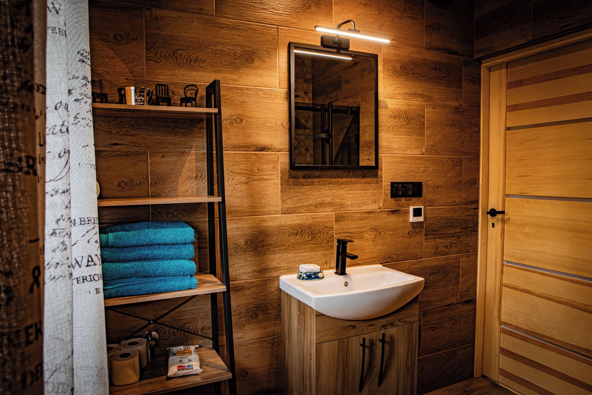 A wooden bathroom with a white sink, a mirror, and shelves with towels.