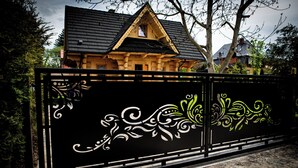 A wooden house with a black roof and a decorative fence with white and green designs.