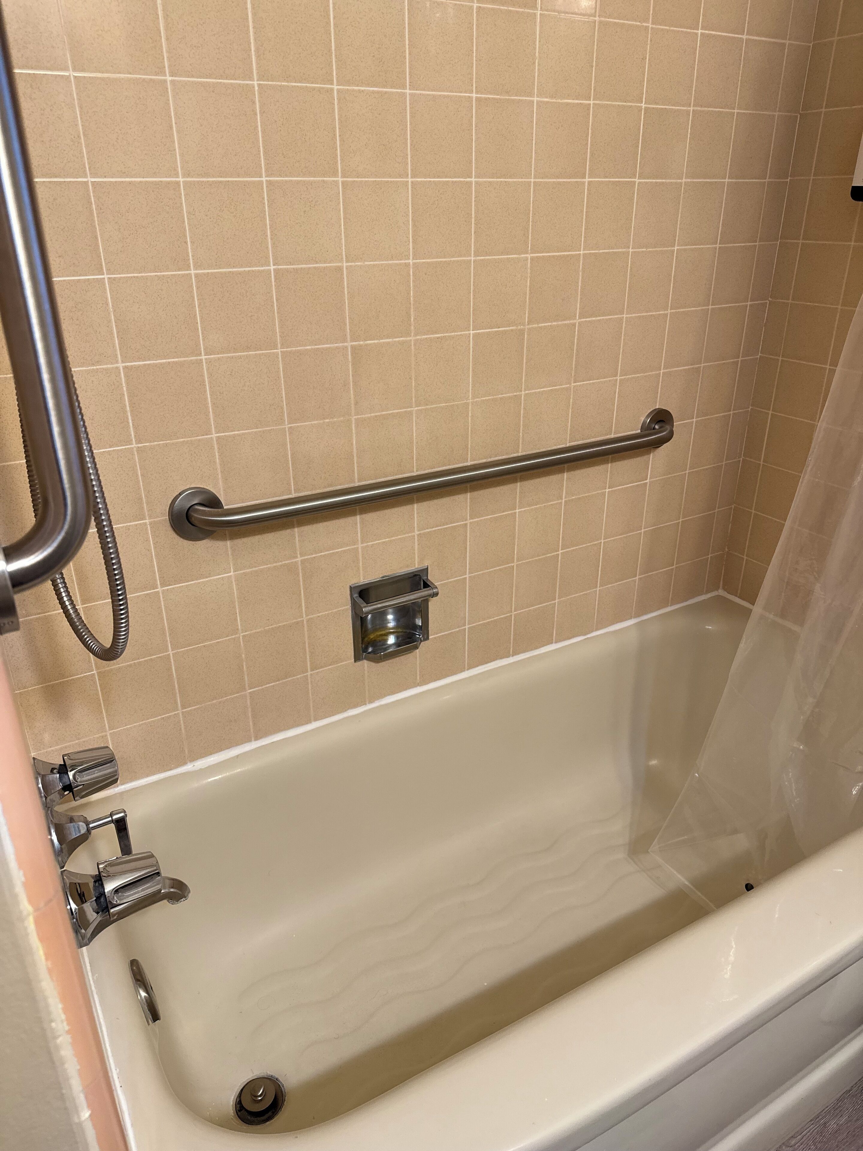 Une baignoire équipée d’une barre d’appui, d’un pommeau de douche à main et d’un robinet.