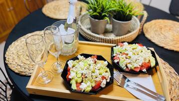 A round dining table with two black plates of salad, a bottle of champagne, and two glasses.