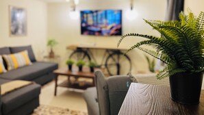 A living room with a sofa, a coffee table, a potted plant, and a bicycle in the background. - Airport Cottage House (Spata-Artemida)
