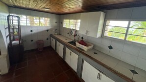 Una cocina con armarios blancos, techo de madera y ventanas con vistas a zonas verdes.