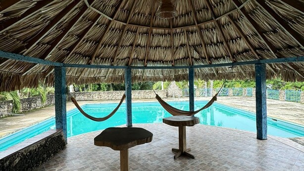 Un pabellón con techo de paja, una piscina y dos hamacas.
