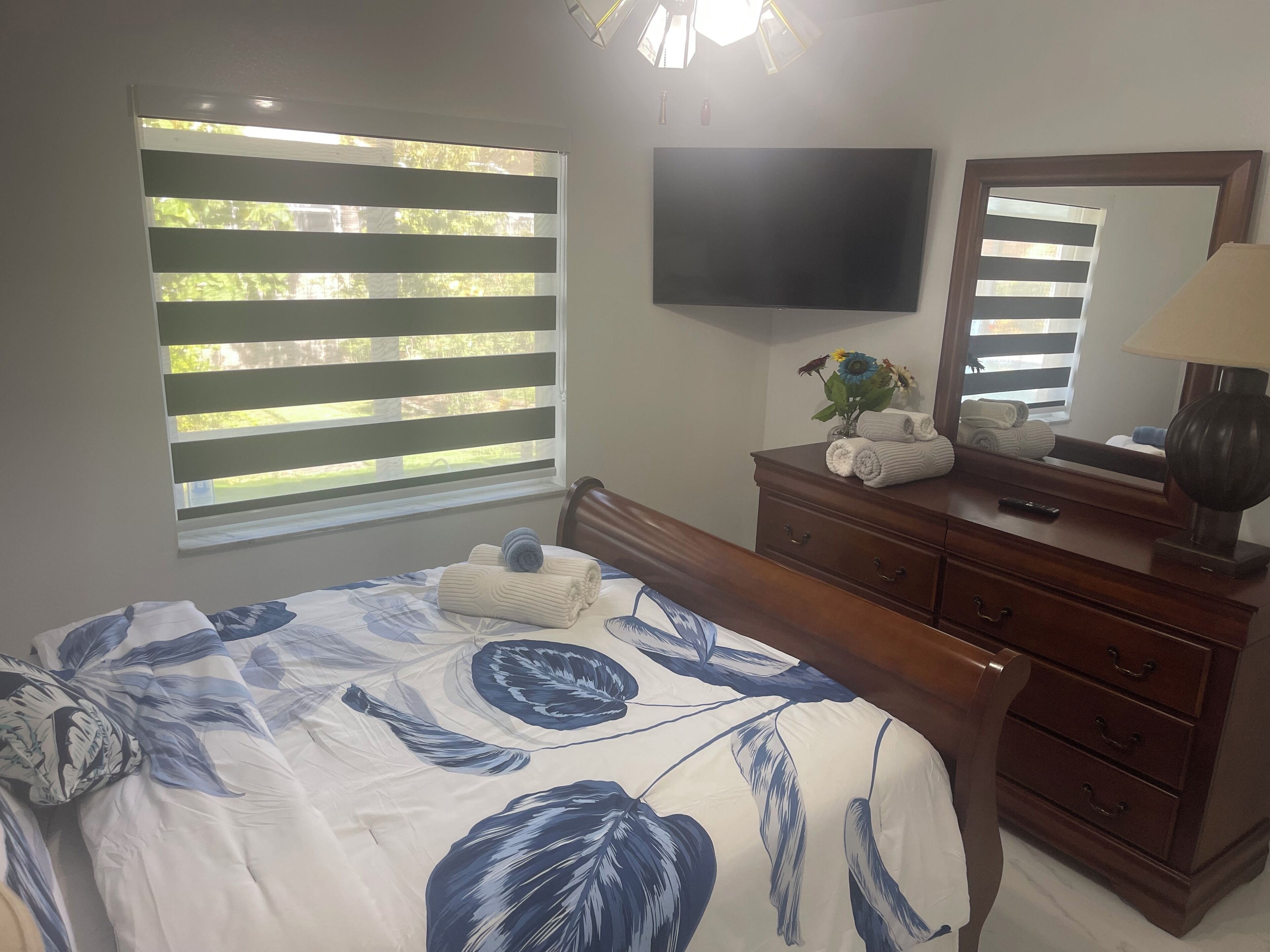 Un dormitorio con cama, cómoda, televisor y ventana con persianas.
