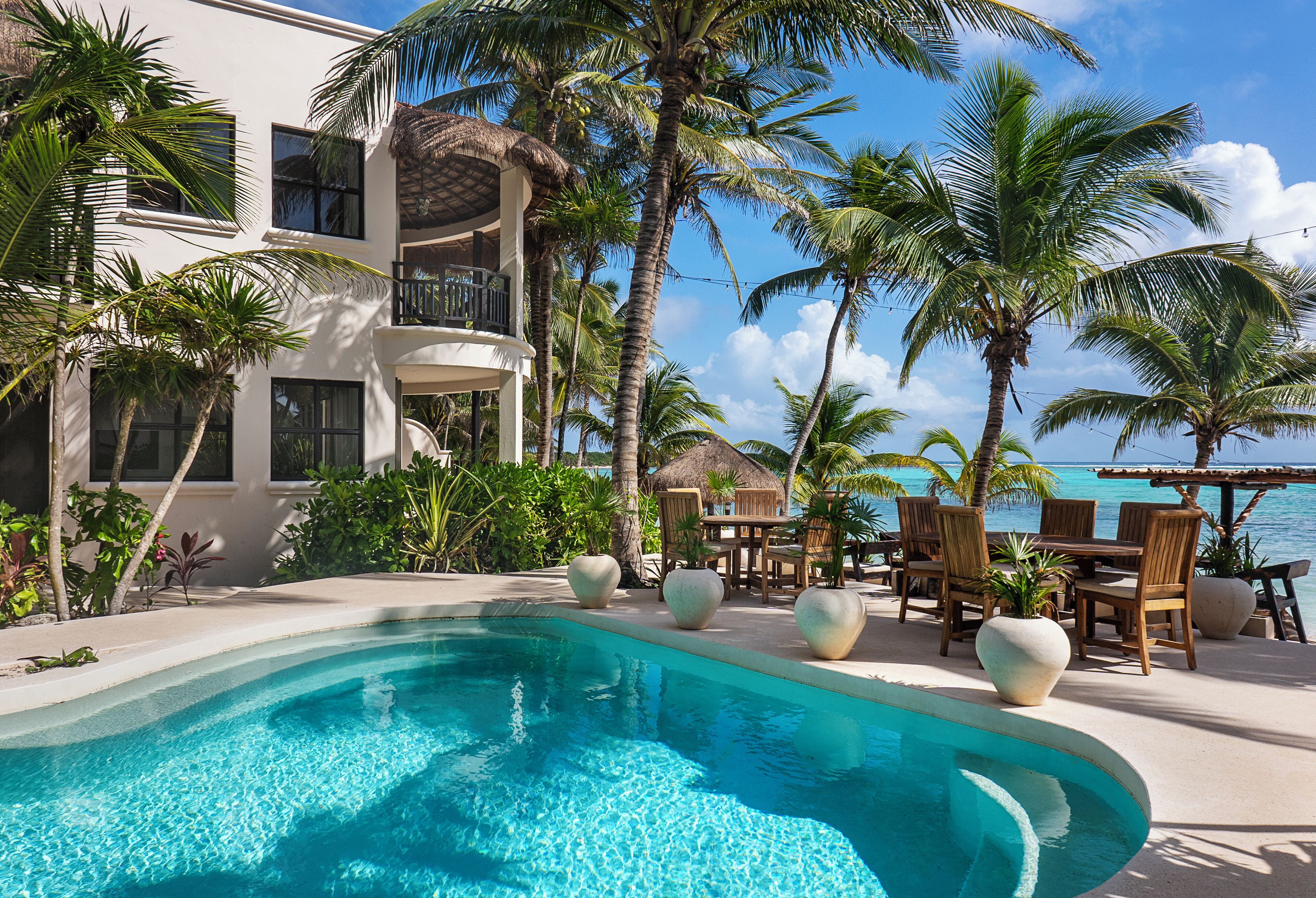 A poolside area with a clear blue pool, palm trees, and a view of the ocean.