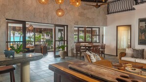 A spacious room with a dining area, a seating area with a sofa, and large windows offering a view of the ocean. - Mantaray Tulum (Tulum)