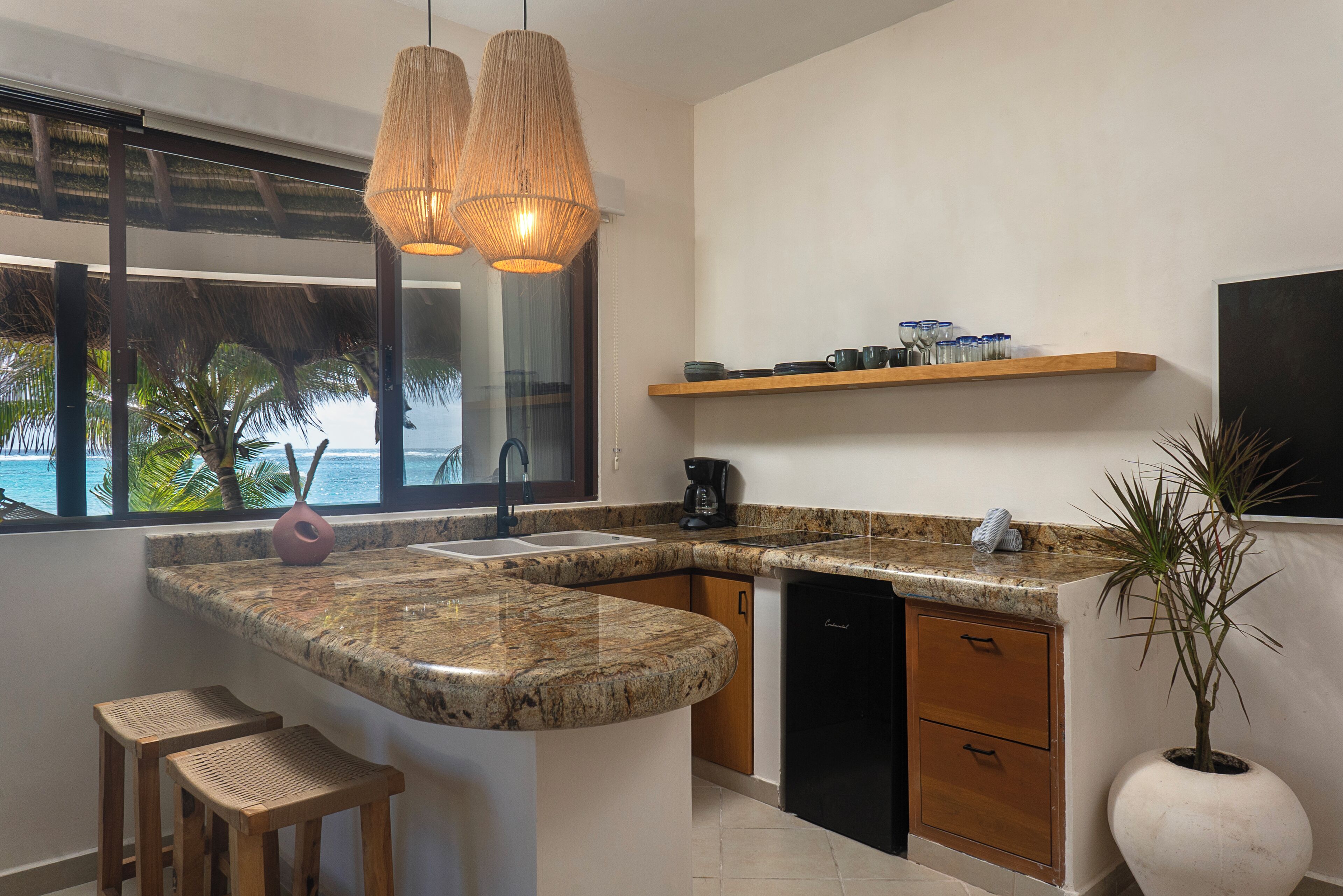 Una cocina con encimeras de granito, taburetes de madera, cafetera y vista al océano.