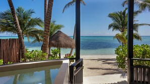 A beach view from a covered area with a pool, palm trees, and a thatched-roof structure. - Mantaray Tulum (Tulum)