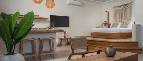 A modern living room with a wooden sofa, a coffee table, and a TV mounted on the wall. There are two wooden stools and a large potted plant.