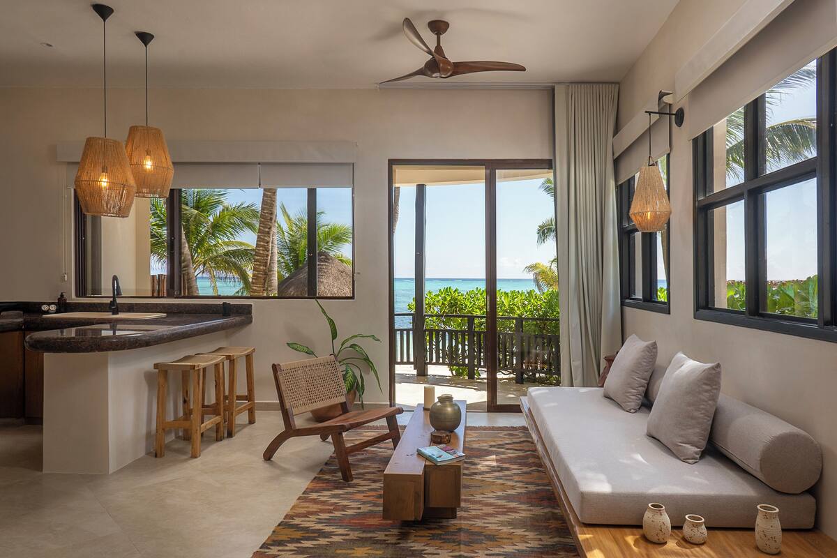 A modern living room with a sofa, a dining area with a bar, and a view of the ocean.