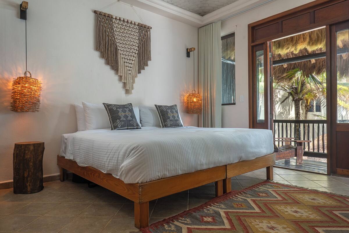 A bed with a wooden frame and white bedding, a woven wall hanging, and a patterned rug.
