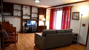 Una sala de estar con suelo de madera, un sofá gris, una silla de madera, un televisor y una lámpara.