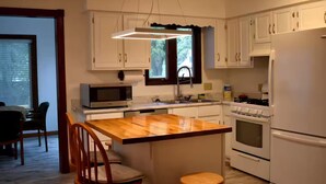 Una cocina con gabinetes blancos, una isla de madera, un microondas, un fregadero y una estufa.
