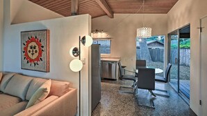 A modern interior with a wooden ceiling, a dining area with a glass table and chairs, a kitchen with stainless steel appliances, and a sliding glass door leading to a backyard. - Mid-Century Steps from Miramar Beach, Private Fenced Garden in Montecito (Montecito)