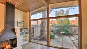 A room with a fireplace, a bookshelf, and a sliding glass door leading to a backyard with a patio and a wooden fence. - Mid-Century Steps from Miramar Beach, Private Fenced Garden in Montecito (Montecito)