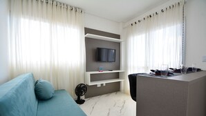Ein modernes Wohnzimmer mit einer Couch, einem an der Wand montierten Fernseher, einem Esstisch mit Stühlen und einem Ventilator.