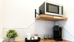 Una cocina con un microondas en un estante de madera, una cafetera, una planta en maceta y una bandeja con tazas y un tarro.