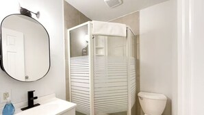 Un baño moderno con ducha envuelta en vidrio, inodoro blanco y lavabo blanco con espejo sobre él.