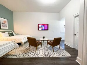 Ein Schlafzimmer mit einem Bett, zwei Stühlen, einem kleinen Tisch und einem an der Wand befestigten Fernseher.