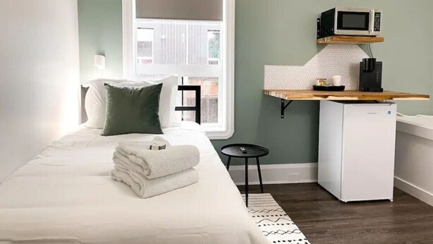 Une chambre à coucher comprenant un lit, des oreillers, une petite table, un four à micro-ondes et un réfrigérateur.