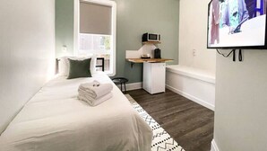 Une chambre à coucher avec un lit, un petit bureau, une télévision et une fenêtre.