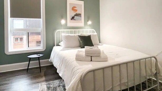 A neatly made bed with white linens, a small bedside table, and a framed picture on the wall.