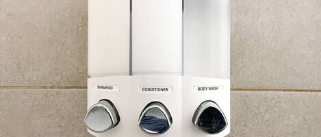 Douche bevestigd aan de muur met drie aparte bedieningen, gelabeld met shampoo, conditioner en douchegel.