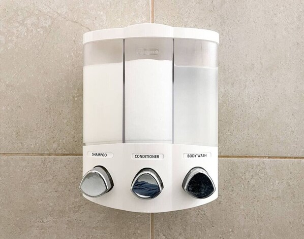 Une douche murale dotée de trois commandes distinctes, étiquetées « shampoing », « après-shampoing » et « gel douche ».