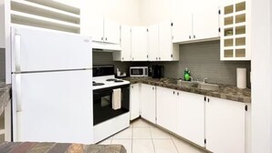 A compact kitchen with white cabinets, a stove, a microwave, and a sink. - Boutique Hotel - #10 Two Double (Thunder Bay)