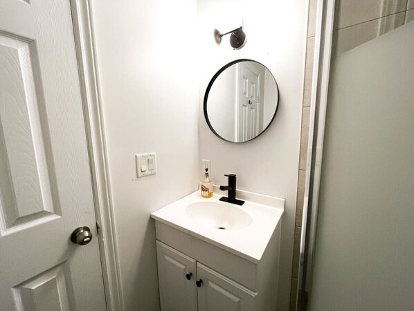 Une salle de bain avec un lavabo blanc, un miroir rond et un flacon de savon pour les mains.