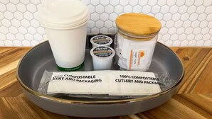 Una bandeja con una taza de café, tarros y cubiertos y envases compostables.