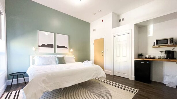 Una habitación de hotel pequeña con una cama, mesitas de noche, un escritorio con microondas y una kitchenette.