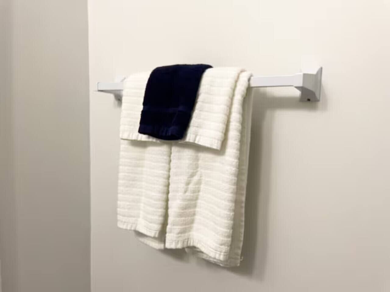 Une serviette blanche, recouverte d’une couverture bleu foncé, est posée sur un porte-serviettes blanc, le tout adossé à un mur uni.