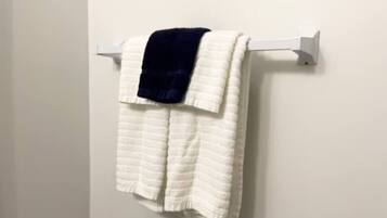 Une serviette blanche, recouverte d’une couverture bleu foncé, est posée sur un porte-serviettes blanc, le tout adossé à un mur uni.