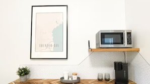 Una cocina con microondas en un estante, cafetera, mapa enmarcado y una mesa de madera con planta y bandeja.