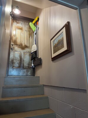 A staircase with a door at the top, a wall-mounted picture, and cleaning tools hanging on the wall.