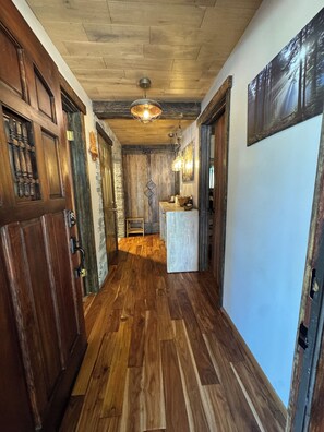 A hallway with wooden flooring, a stone wall, and a wooden door with a glass panel. - Beautiful Yo Mama’s GuestHouse (Wrightwood)