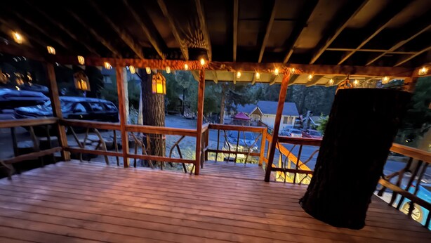 Une terrasse en bois avec une rambarde, des guirlandes lumineuses et une vue sur un parking et des bâtiments en arrière-plan.