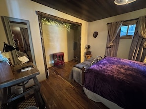 Um quarto com uma cama, uma escrivaninha, um espelho e um pequeno armário.