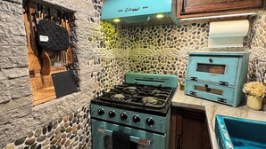 Une cuisine avec un mur en pierre, un poêle ancien, des ustensiles en bois et un meuble bleu.