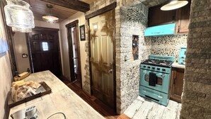 Une cuisine avec un mur en pierre, un poêle d’époque et des poutres en bois au plafond.