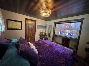 A bedroom with a bed, a television displaying a movie, and a wooden ceiling.