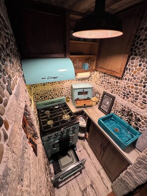 Een compacte keuken met een retro fornuis, een blauwe gootsteen en een backsplash van natuursteen.