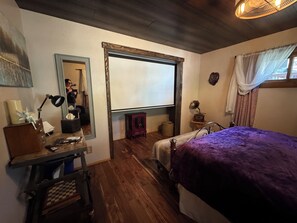 Een slaapkamer met een bed, een bureau, een spiegel en een raam met gordijnen.