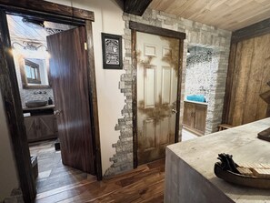 A rustic bathroom with a stone wall, wooden door, and a large mirror. - Beautiful Yo Mama’s GuestHouse (Wrightwood)